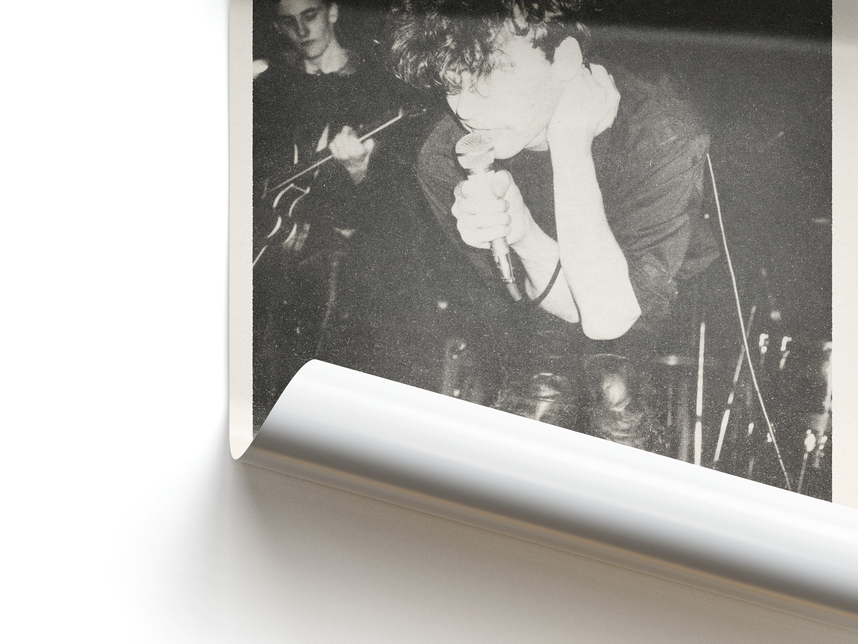 Black and white photo of a person singing into a microphone with another person playing guitar.